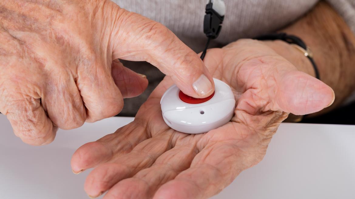 Manos de persona mayor presionando el botón rojo de teleasistencia