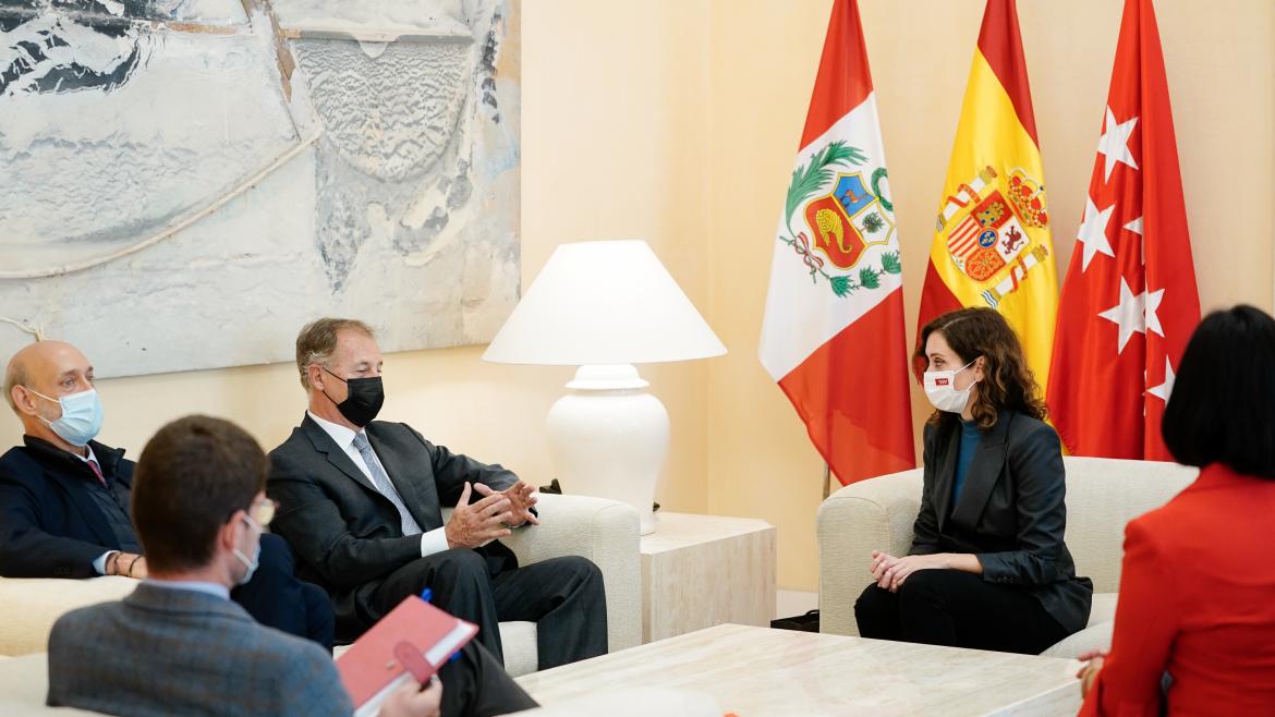 La presidenta y el alcalde de Lima sentados en unos sofás conversando y acompañados de otros miembros