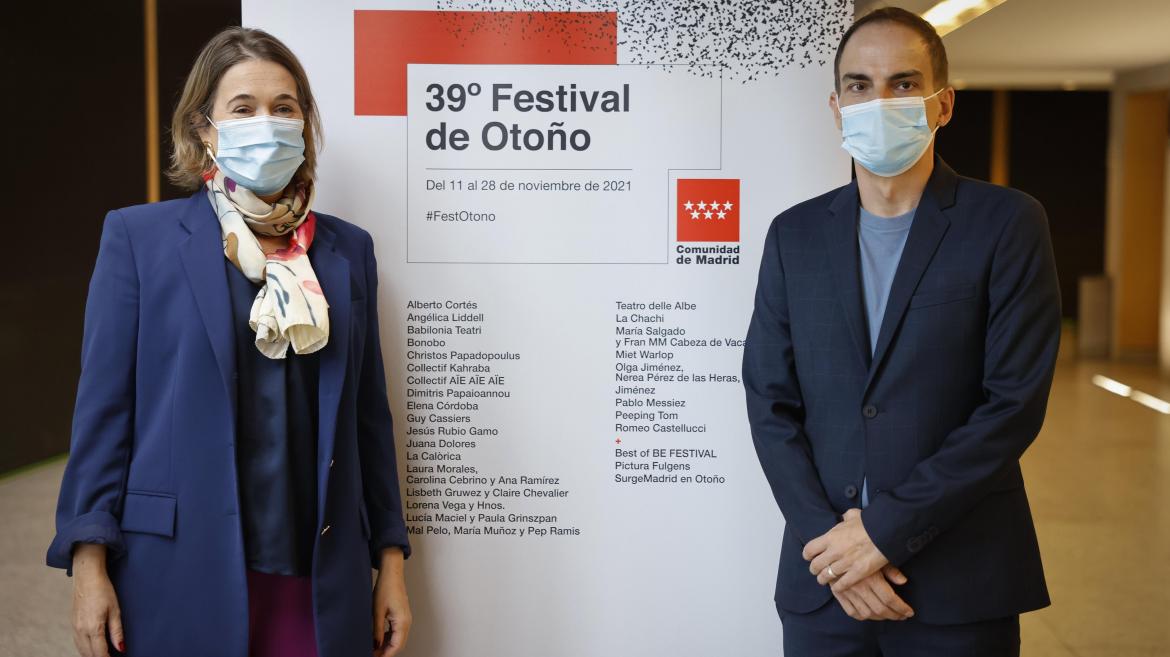 Dos personas posan con el cartel de actuaciones del festival de otoño