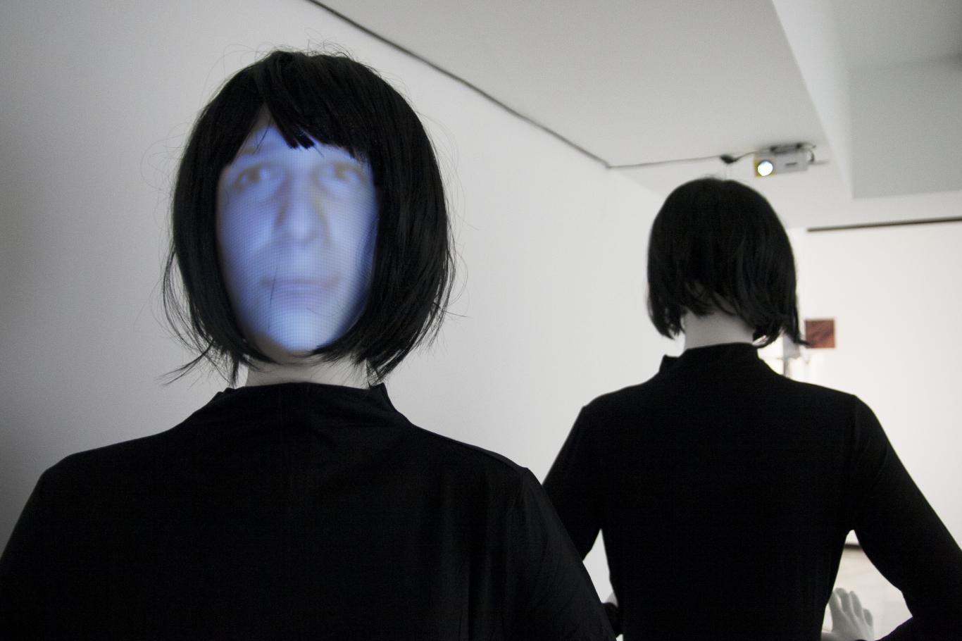 Two mannequins with black wigs and face projections on their faces