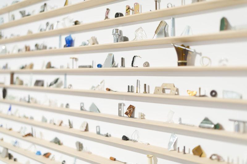 Artistic installation made with small wooden shelves arranged horizontally with small objects on them
