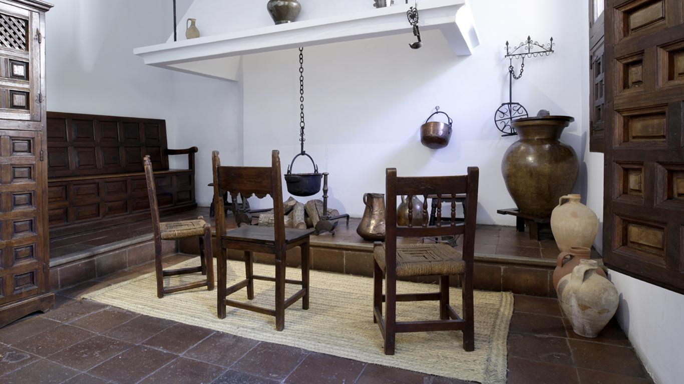 Cocina antigua con chimenea, dos sillas de madera y objetos de hierro y latón