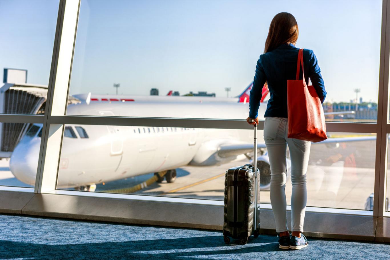 Mujer de espaldas mirando un avión desde las ventanas de la terminal del aeropuerto