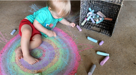 Un niño pequeño juega en el suelo con tizas de colores