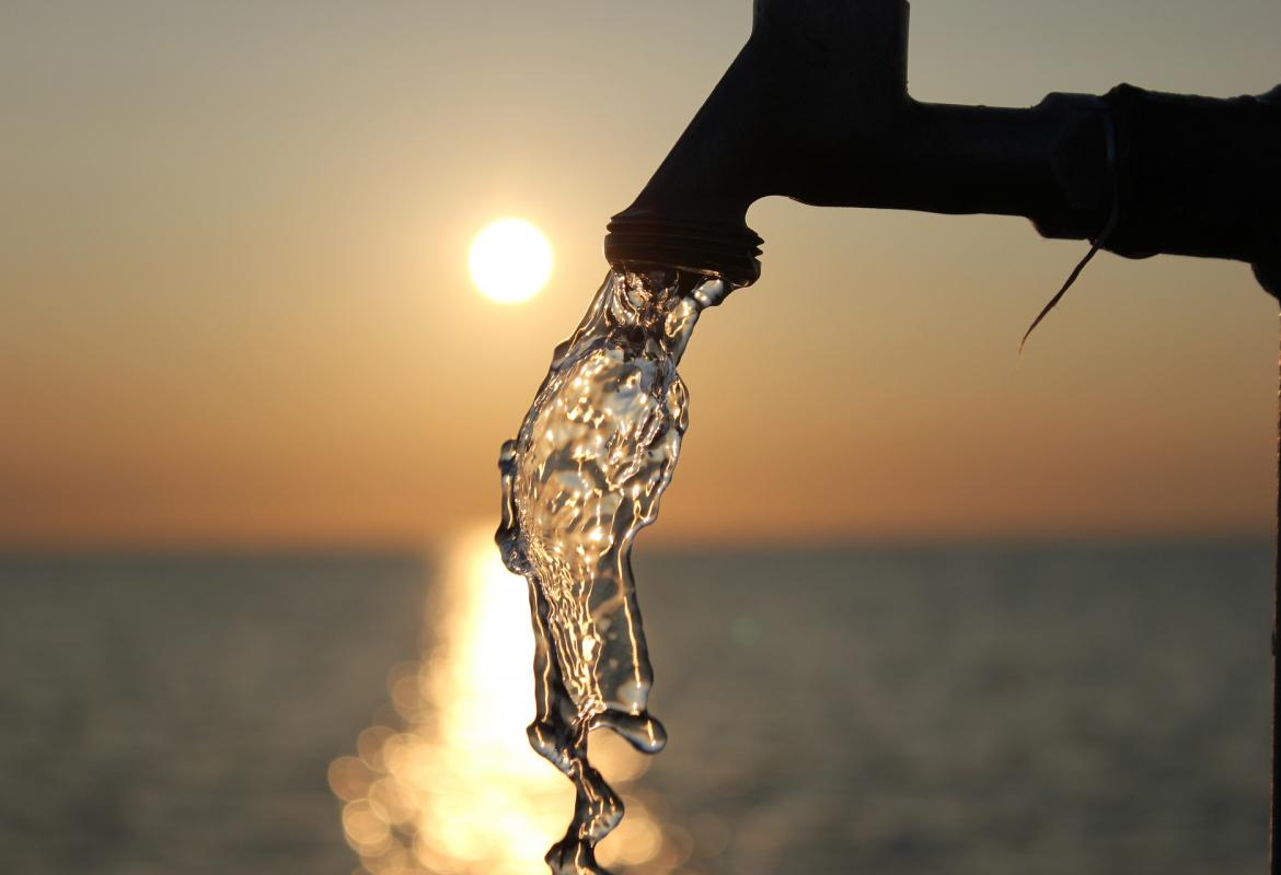 agua saliendo de un grifo con el atardecer de fondo