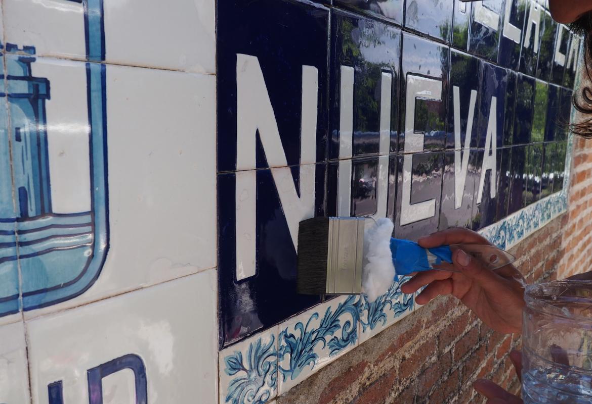 una barniza con brocha azulejos azules con la palabra en blanco Nueva, enmarcada en cenefa de flores